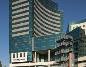 Exterior view of Prima Millennium, a modern multi-storey building with curved green-tinted glass façades, beige horizontal accents, and commercial spaces at street level.