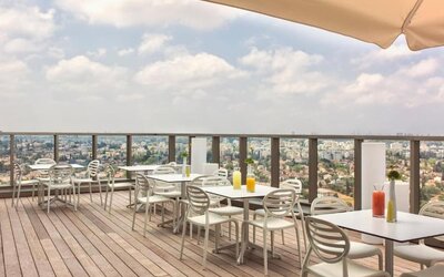 Rooftop dining terrace with wooden decking, white tables and chairs, parasols, and panoramic city views at Prima Millennium.