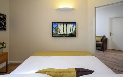Close-up view of a neatly made king-size bed with white bedding, a gold bed runner, and contrasting decorative cushions at Prima Park Hotel.
