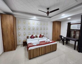 Guest bedroom with a wooden double bed, white bedding, red decorative cushions and bed runner, patterned feature wall, wardrobes, ceiling fan, and a small table with chairs beside the window at Hotel Urban Abode.