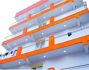 Exterior view of the multi-storey hotel building featuring white walls, bright orange balcony accents, metal railings, and balconies overlooking the surrounding area.