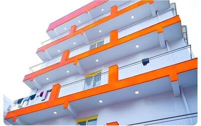Exterior view of the multi-storey hotel building featuring white walls, bright orange balcony accents, metal railings, and balconies overlooking the surrounding area.