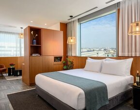 King bed with white bedding, teal runner, wood-panelled walls and city views at Prima Link.