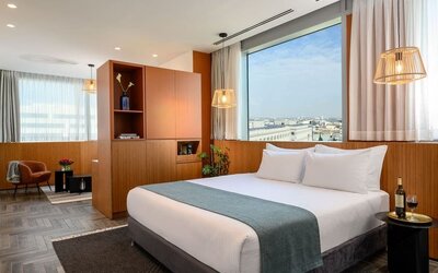 King bed with white bedding, teal runner, wood-panelled walls and city views at Prima Link.