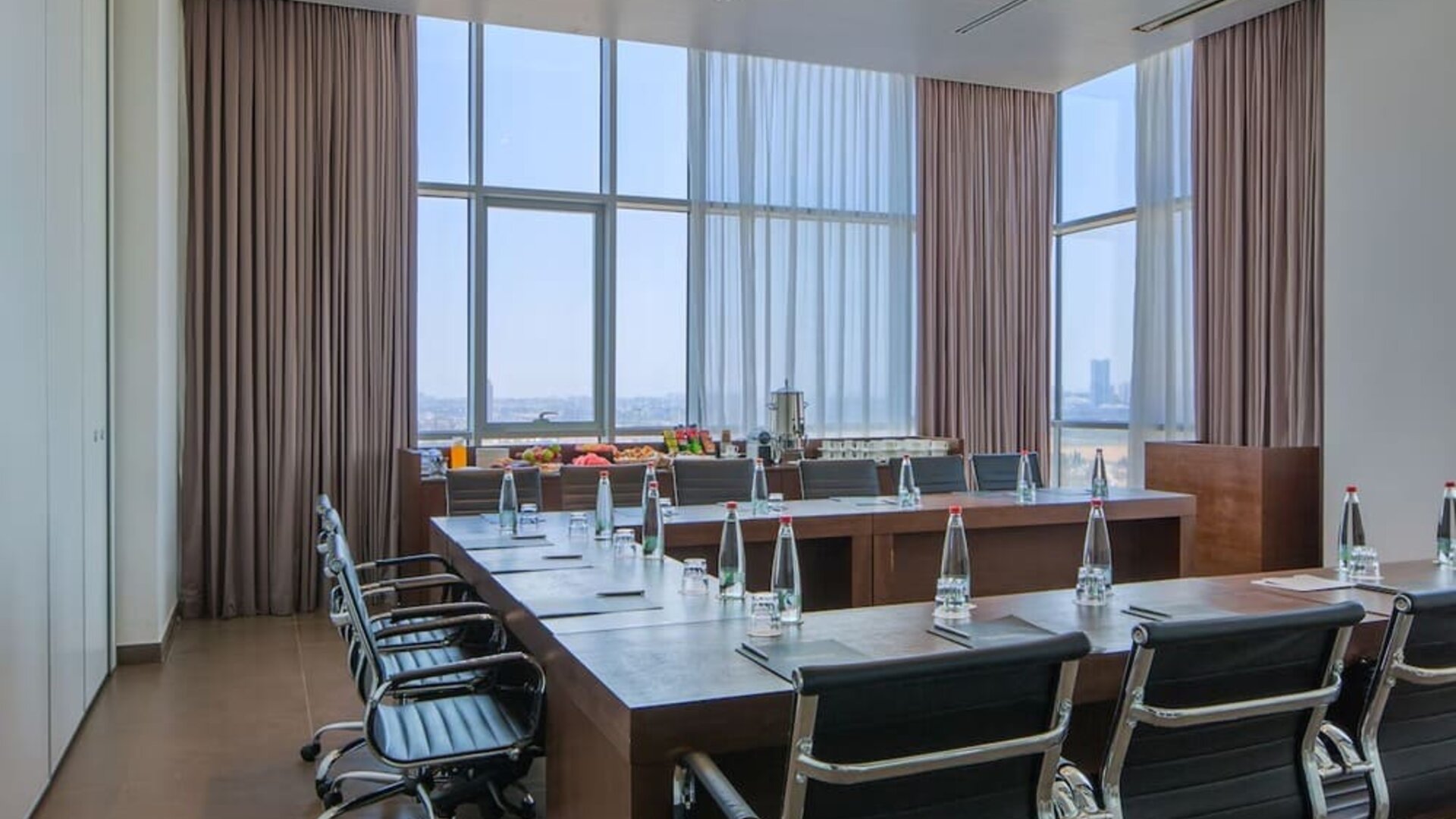 Boardroom with a long conference table, black chairs, bottled water and city views  at Prima Link.