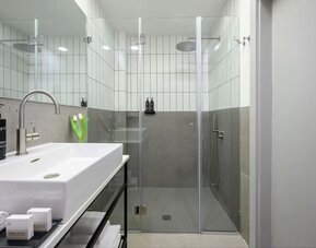 Walk-in shower with glass doors, rainfall showerhead, tiled walls and white vanity at Prima Link.