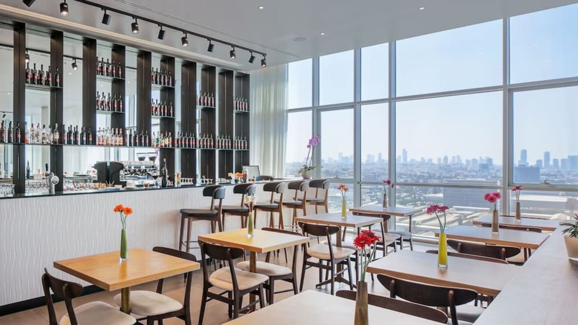 Restaurant with wooden tables, flower vases, wine shelves and panoramic windows at Prima Link.