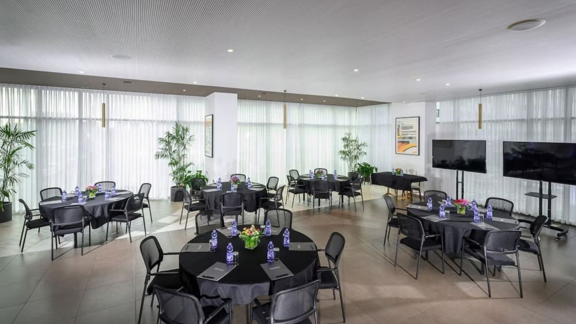 Meeting space with round tables, black tablecloths, chairs and floor-to-ceiling curtains at Prima Link.