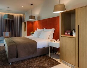 Spacious guest room with a king bed, brown throw, orange headboard and wooden cabinetry at Prima Link.