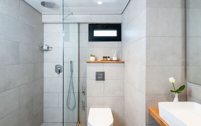 Modern bathroom with a glass-enclosed shower, rainfall showerhead and stone-effect tiles at Prima Galil Tiberias.