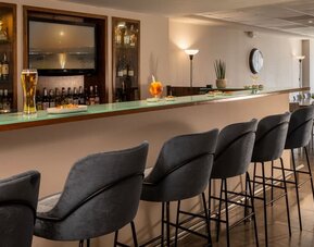 Hotel bar with a long counter, grey upholstered stools and a display of drinks at Prima Galil Tiberias.