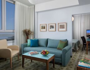 Suite living area with a turquoise sofa, colourful cushions and scenic views through large windows at Prima Galil Tiberias.