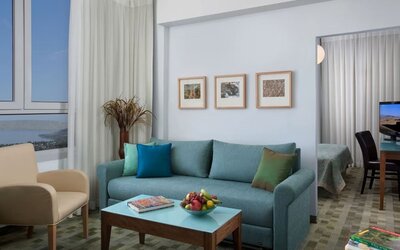 Suite living area with a turquoise sofa, colourful cushions and scenic views through large windows at Prima Galil Tiberias.