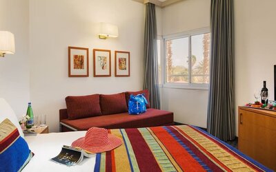 Guest bedroom with a colourful striped bedspread, red sofa, framed artwork and a flat-screen television at Prima Music Eilat.