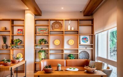 Lounge seating area with an orange sofa, wooden shelving, decorative objects and indoor plants at Prima Music Eilat.