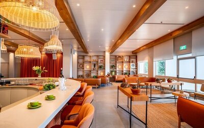 Restaurant and lounge area with orange bar stools, woven pendant lights, wooden ceiling beams and contemporary seating at Prima Music Eilat.