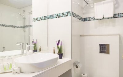 Bathroom with a white vessel sink, large mirror, chrome fixtures and blue-and-green mosaic tile accents at Prima Music Eilat.
