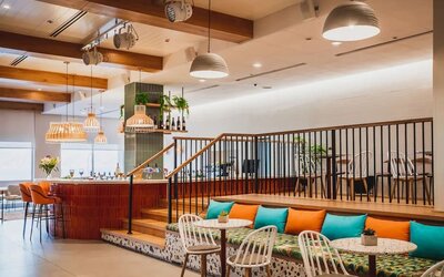 Restaurant lounge with a raised seating area, orange and turquoise cushions, woven chairs and pendant lighting at Prima Music Eilat.