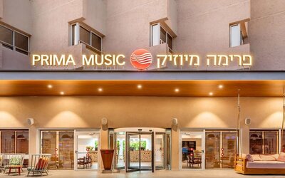 Exterior entrance to Prima Music Eilat, featuring illuminated hotel signage and glass entrance doors.
