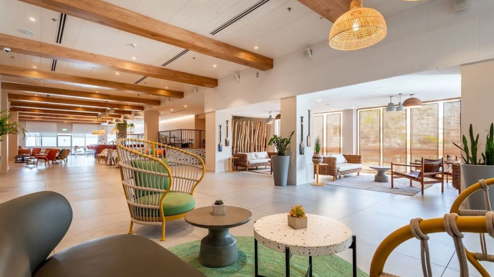 Spacious hotel lobby with wooden ceiling beams, decorative shelving, plants and contemporary seating at Prima Music Eilat.