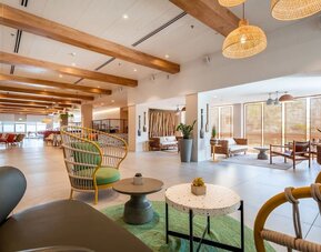 Spacious hotel lobby with wooden ceiling beams, decorative shelving, plants and contemporary seating at Prima Music Eilat.