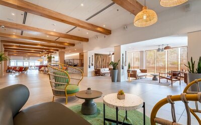 Spacious hotel lobby with wooden ceiling beams, decorative shelving, plants and contemporary seating at Prima Music Eilat.