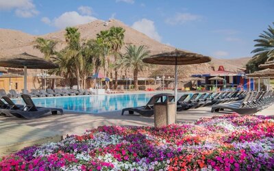 Outdoor swimming pool surrounded by sun loungers, parasols, palm trees and colourful flower beds at Prima Music Eilat.