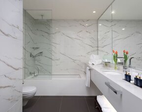 Bathroom with marble-effect walls, bathtub, glass shower screen and double vanity at Lady Stern Hotel.