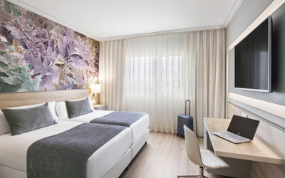 Guest room with twin beds, grey bedding, a work desk, open suitcase and decorative botanical wall art at Hotel Sallés Ciutat del Prat.