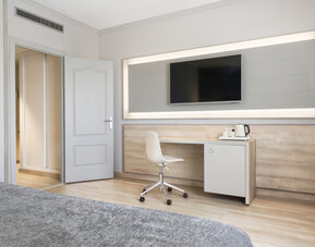Guest room workspace with a desk, white chair, wall-mounted television and tea-making facilities at Hotel Sallés Ciutat del Prat.