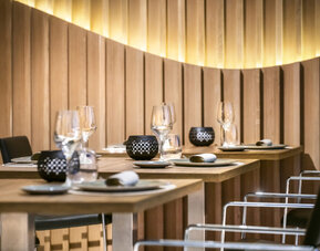 Restaurant tables set with plates, glasses and black chairs beside a softly illuminated wooden feature wall at Hotel Sallés Ciutat del Prat.