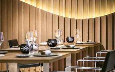 Restaurant tables set with plates, glasses and black chairs beside a softly illuminated wooden feature wall at Hotel Sallés Ciutat del Prat.