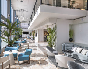 Spacious hotel lobby with grey sofas, modern armchairs, indoor plants and polished marble flooring at Hotel Sallés Ciutat del Prat.