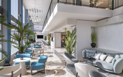 Spacious hotel lobby with grey sofas, modern armchairs, indoor plants and polished marble flooring at Hotel Sallés Ciutat del Prat.