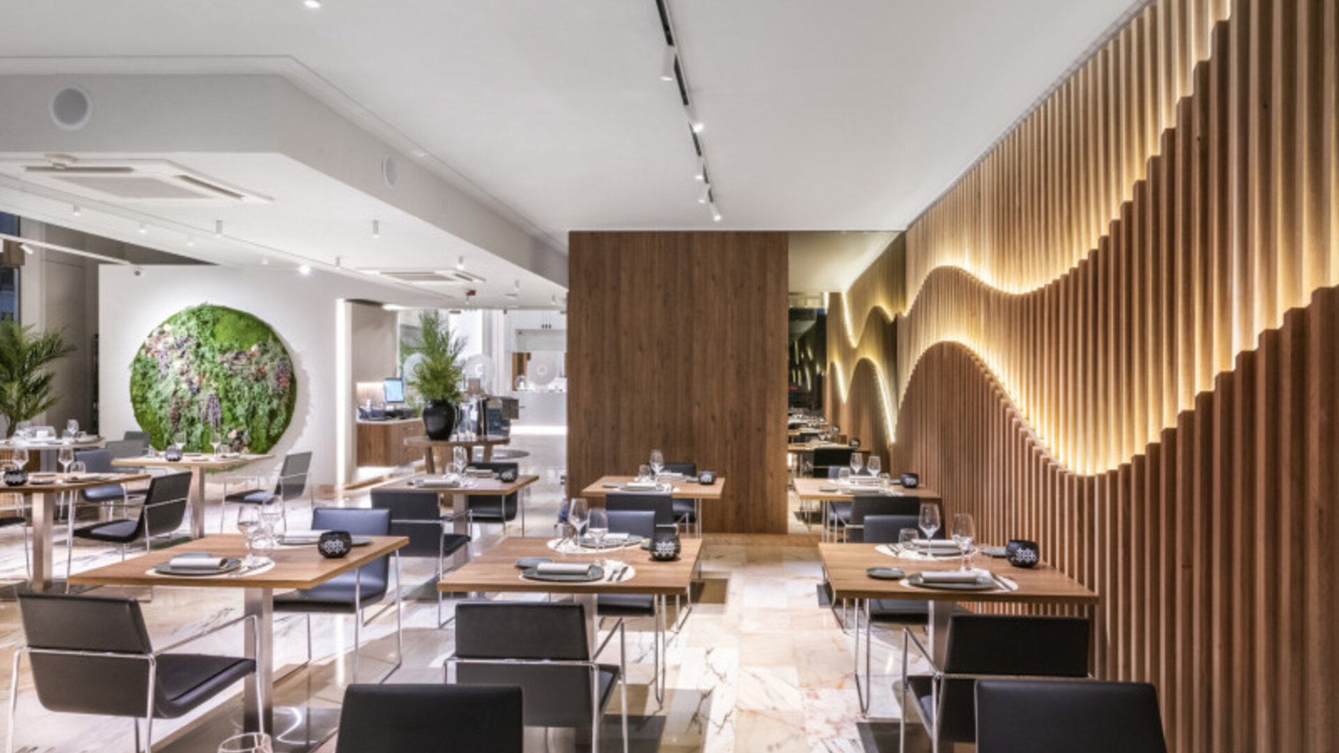 Contemporary restaurant interior with neatly arranged tables, black chairs, indoor plants and wooden wall panels at Hotel Sallés Ciutat del Prat.
