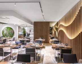 Contemporary restaurant interior with neatly arranged tables, black chairs, indoor plants and wooden wall panels at Hotel Sallés Ciutat del Prat.