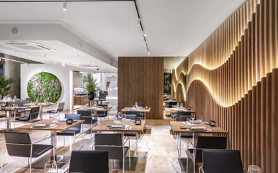 Contemporary restaurant interior with neatly arranged tables, black chairs, indoor plants and wooden wall panels at Hotel Sallés Ciutat del Prat.