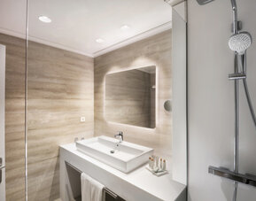 Modern bathroom with a glass shower enclosure, white vanity basin, illuminated mirror and beige tiled walls at Hotel Sallés Ciutat del Prat.