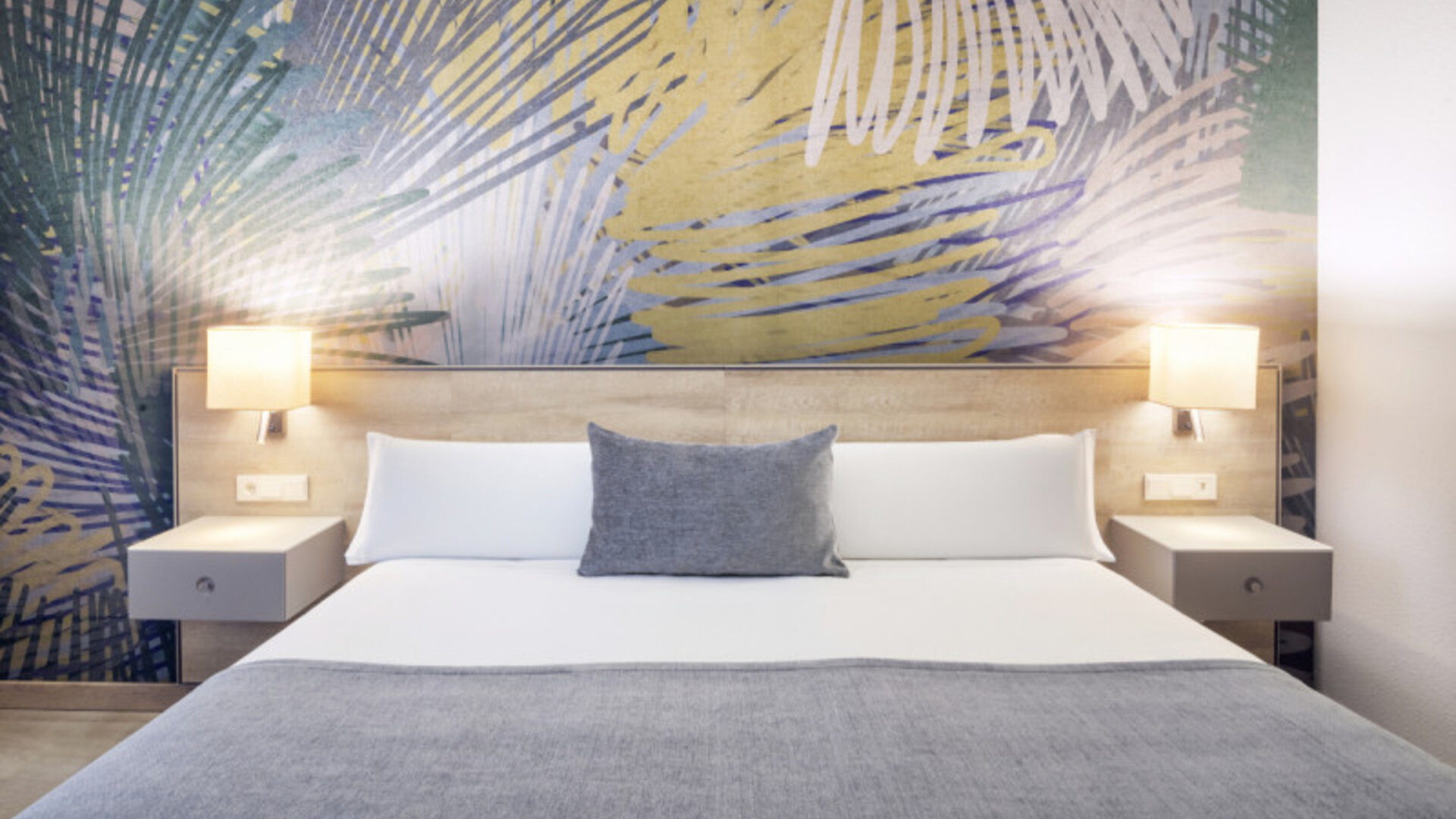 Double bed dressed in white linens and grey accents, flanked by bedside tables and wall lamps at Hotel Sallés Ciutat del Prat.