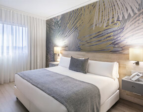 Guest bedroom with a king-size bed, grey bedding, white curtains and a colourful abstract feature wall at Hotel Sallés Ciutat del Prat.