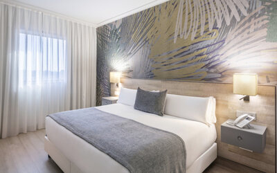 Guest bedroom with a king-size bed, grey bedding, white curtains and a colourful abstract feature wall at Hotel Sallés Ciutat del Prat.