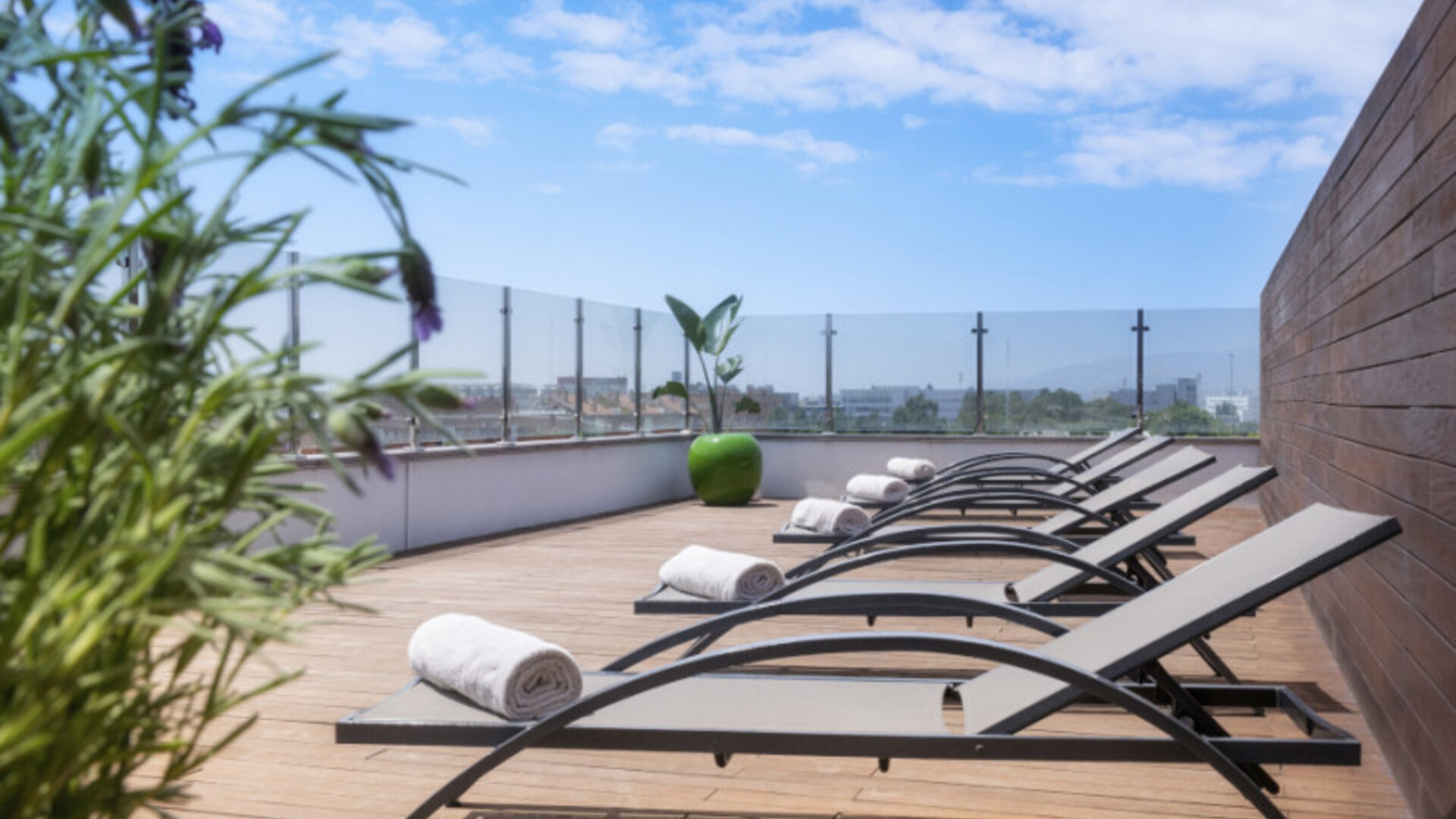 Rooftop sun deck with reclining loungers, rolled white towels, wooden flooring and glass railings at Hotel Sallés Ciutat del Prat.