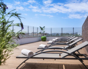 Rooftop sun deck with reclining loungers, rolled white towels, wooden flooring and glass railings at Hotel Sallés Ciutat del Prat.
