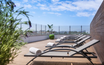 Rooftop sun deck with reclining loungers, rolled white towels, wooden flooring and glass railings at Hotel Sallés Ciutat del Prat.