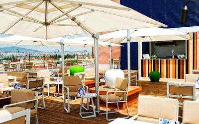 Rooftop terrace with white parasols, wooden tables, outdoor seating and city views at Hotel Sallés Ciutat del Prat.