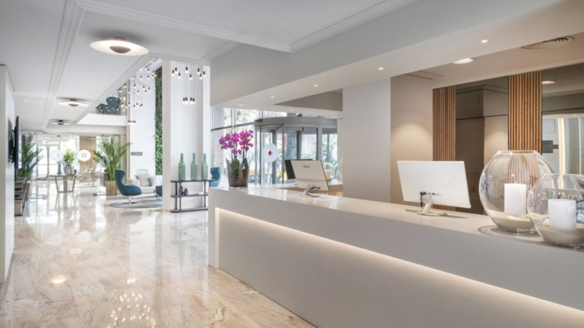 Bright reception desk with marble flooring, white counters, decorative plants and pendant lighting at Hotel Sallés Ciutat del Prat.