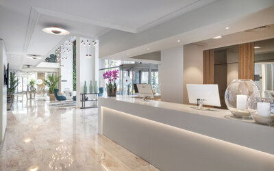 Bright reception desk with marble flooring, white counters, decorative plants and pendant lighting at Hotel Sallés Ciutat del Prat.