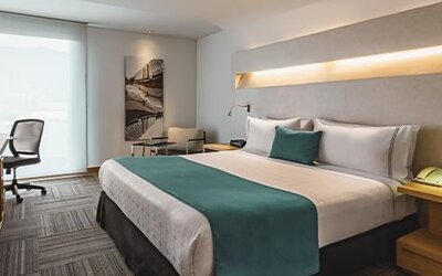 Guest room with king-size bed, teal cushions, bedside furniture and workspace at Sonesta Hotel Bogotá.