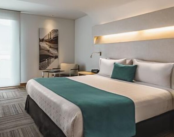 Guest room with king-size bed, teal cushions, bedside furniture and workspace at Sonesta Hotel Bogotá.