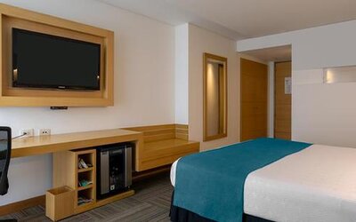 Guest room with white bedding, teal bed runner, wall-mounted television and work desk at Sonesta Hotel Bogotá.